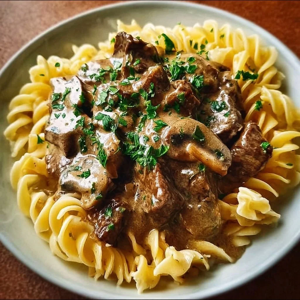 Hearty slow cooker beef stroganoff served with noodles and garnished with parsley